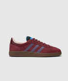 Red suede sneaker with purple stripes, brown sole, side profile on white background