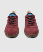 Red suede Adidas sneakers with purple stripes and gum sole, front view on white background