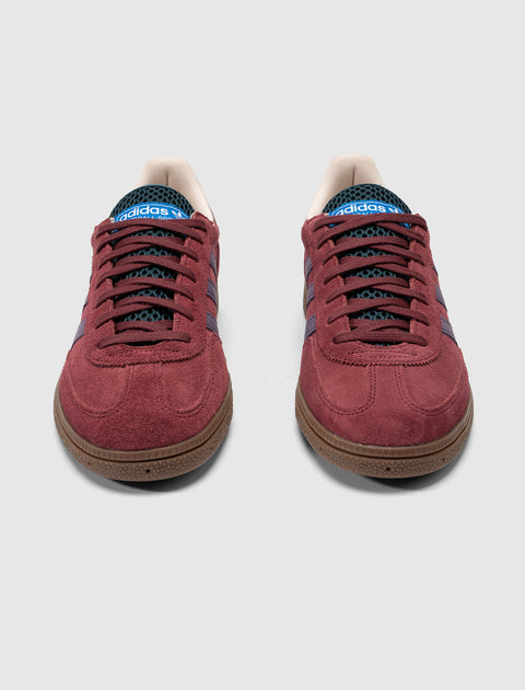 Red suede Adidas sneakers with purple stripes and gum sole, front view on white background