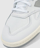 Close-up of white and grey sneaker with mesh and leather materials, detailed stitching, and laces.