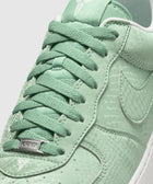 Mint green low-top sneaker with snakeskin texture, white sole, and signature logo details.