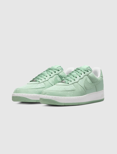 Light green low-top sneakers with textured leather and white sole on gray background