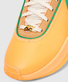 Close-up of orange and tan sneaker with green trim, white laces, and gold XX lace charm