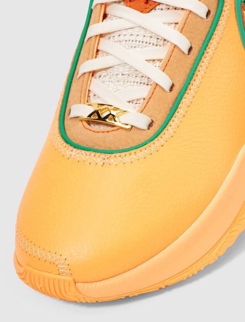 Close-up of orange and tan sneaker with green trim, white laces, and gold XX lace charm