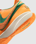 Close-up of orange sneaker with green accents, textured sole, and stitched Swoosh logo