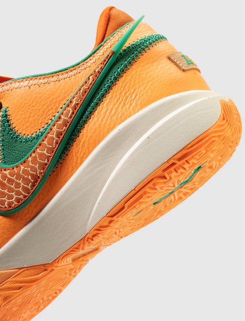 Close-up of orange sneaker with green accents, textured sole, and stitched Swoosh logo