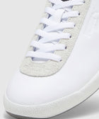 Close-up of white sneaker with suede trim, textured sole, and white laces