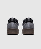 Back view of black and grey suede low-top sneakers with textured brown soles on white background