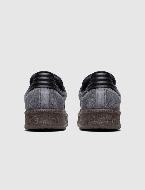 Back view of black and grey suede low-top sneakers with textured brown soles on white background