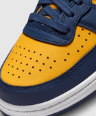 Close-up of a yellow and navy blue leather sneaker with perforated toe box and white sole