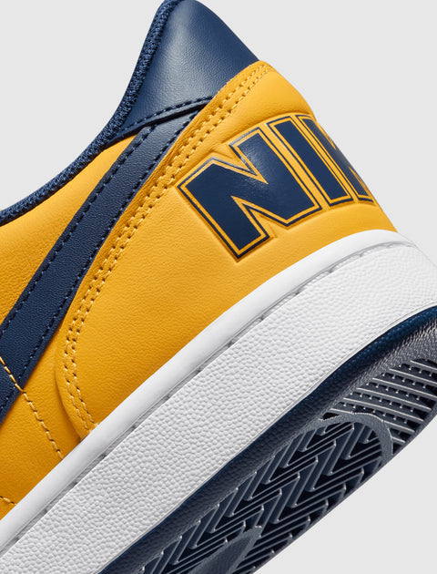 Close-up of yellow and navy low-top sneaker with bold logo on the heel and white sole