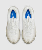 Top view of white athletic sneakers with chunky soles and blue insoles on a neutral background.