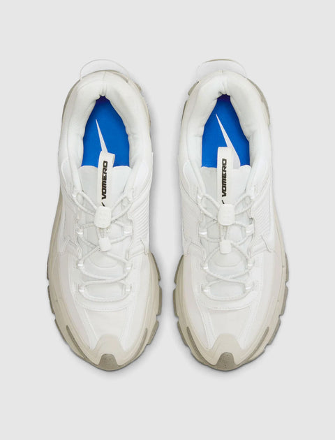 Top view of white athletic sneakers with chunky soles and blue insoles on a neutral background.