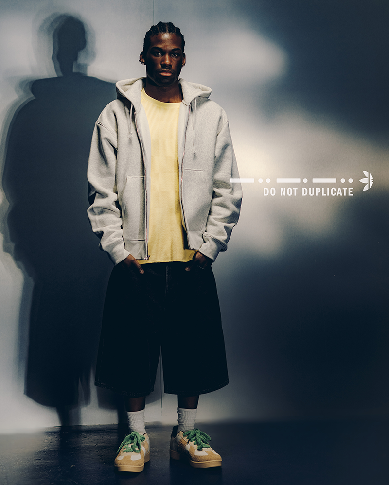 Man wearing gray hoodie, yellow shirt, black wide shorts, and sneakers in streetwear style