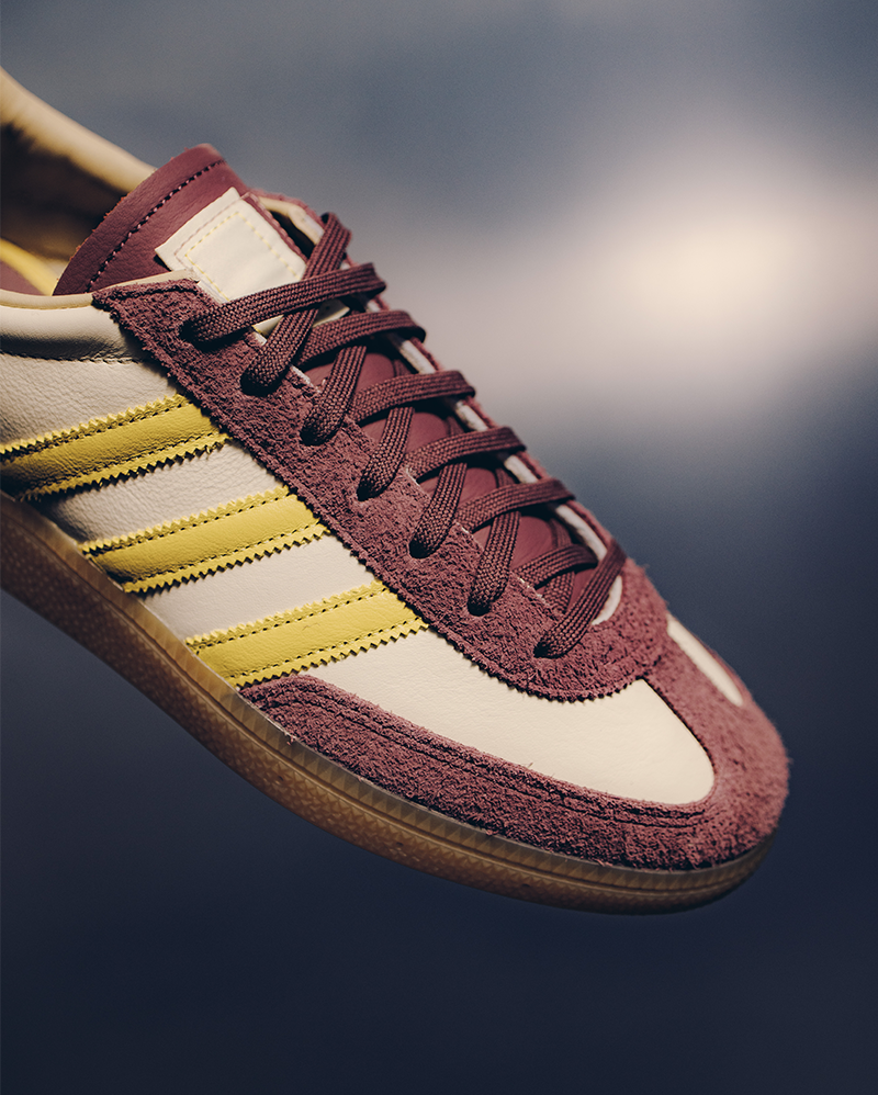 Close-up of a men's sneaker with burgundy suede, yellow stripes, and gum sole
